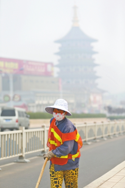 近日，在古都洛陽，環(huán)衛(wèi)工人身后的“天堂”被霧霾籠罩著。