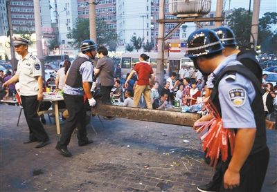 6月13日晚8點(diǎn)，朝陽路和青年路交叉口西側(cè)，一次聯(lián)合執(zhí)法行動(dòng)中，輔警與協(xié)管抬走商戶的燒烤用具。新京報(bào)記者 尹亞飛 攝