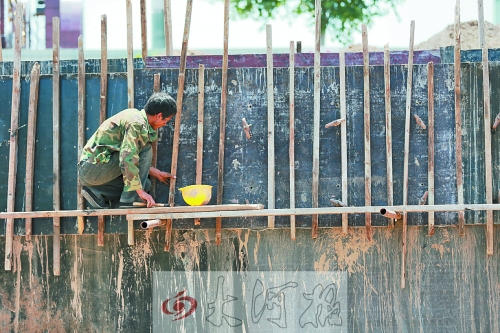 　　烈日下，狹窄的架子上，工人正用錘子固定樁基。