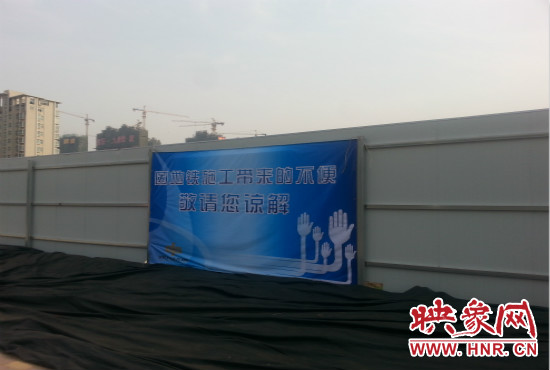 道路南側(cè)圍起了白色的圍擋，墻上標(biāo)示著“因地鐵施工帶來的不便敬請您諒解”的提示牌。