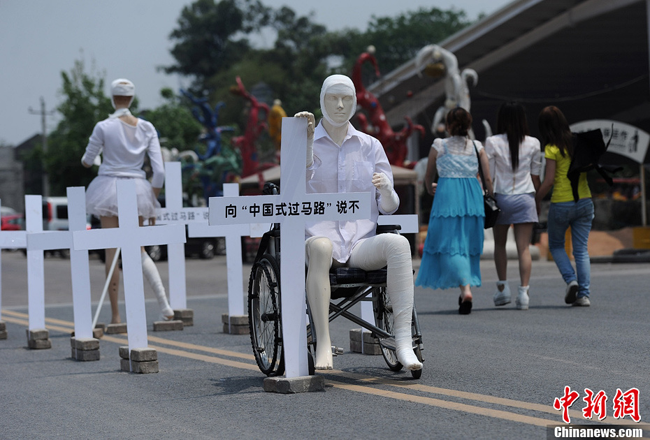 4月16日，重慶市洋人街上擺放著兩個受了傷的塑料人像“模特”，旁邊十字架上寫著向“中國式過馬路”說不