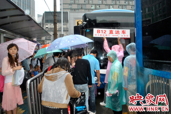 公交志愿者雨中高舉“B12-直達車”指示牌疏導(dǎo)返校學生乘車