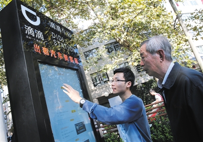10月15日，滴滴工作人員（左）指導乘客使用“滴滴車站”的電子屏預約出租車。