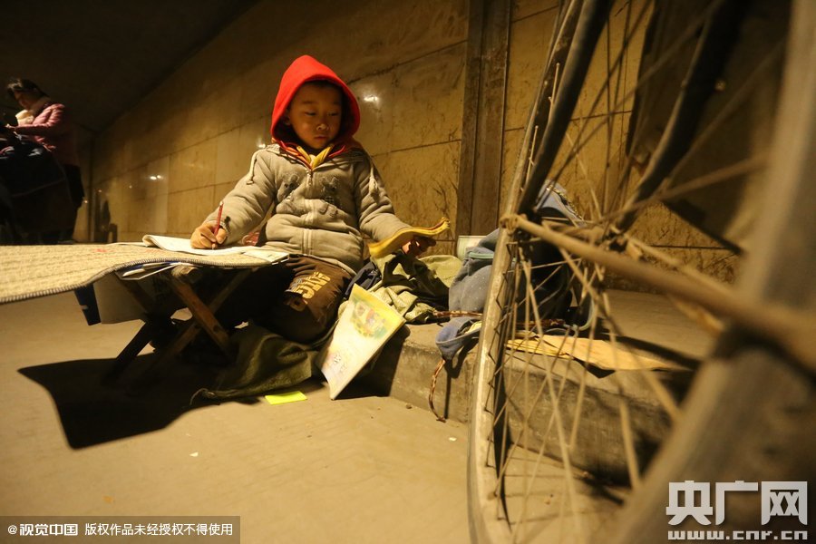 2015年11月8日晚，鄭州，7歲男孩涵洞橋下陪父母練攤，路邊燈下坐小馬扎上寫作業(yè)。