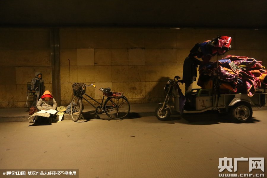 2015年11月8日晚，鄭州，7歲男孩涵洞橋下陪父母練攤，路邊燈下坐小馬扎上寫作業(yè)。