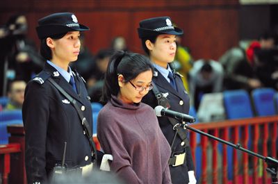 被告人盧梅低著頭，站在朝陽(yáng)法院刑事審判庭的被告席上。