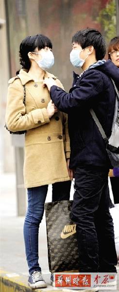 公交站臺(tái)上，一對(duì)年輕人戴著口罩，系緊衣領(lǐng)。